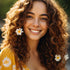 A person with curly hair adorned with small white flowers smiles at the camera, wearing a yellow floral-patterned outfit.