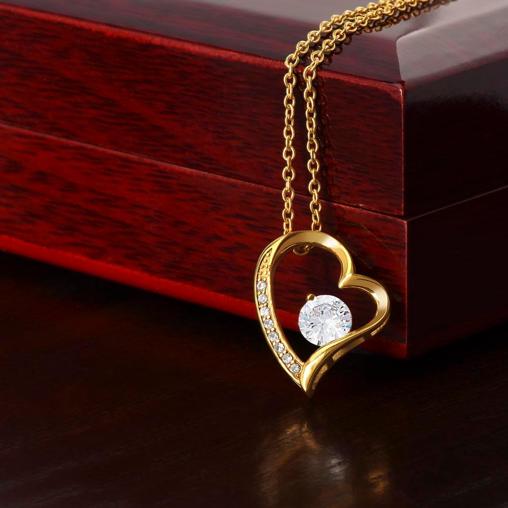 The Forever Love Necklace by ShineOn Fulfillment features a heart-shaped design embellished with a large clear gem and smaller gems on one side, beautifully displayed in a wooden box. Its elegant white gold finish enhances its timeless beauty.