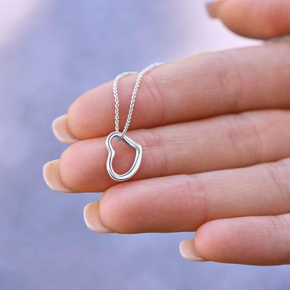 A hand holds a Delicate Heart Necklace by Divine Dispatch, crafted in sterling silver, with its heart-shaped pendant gleaming softly against a blurred background.