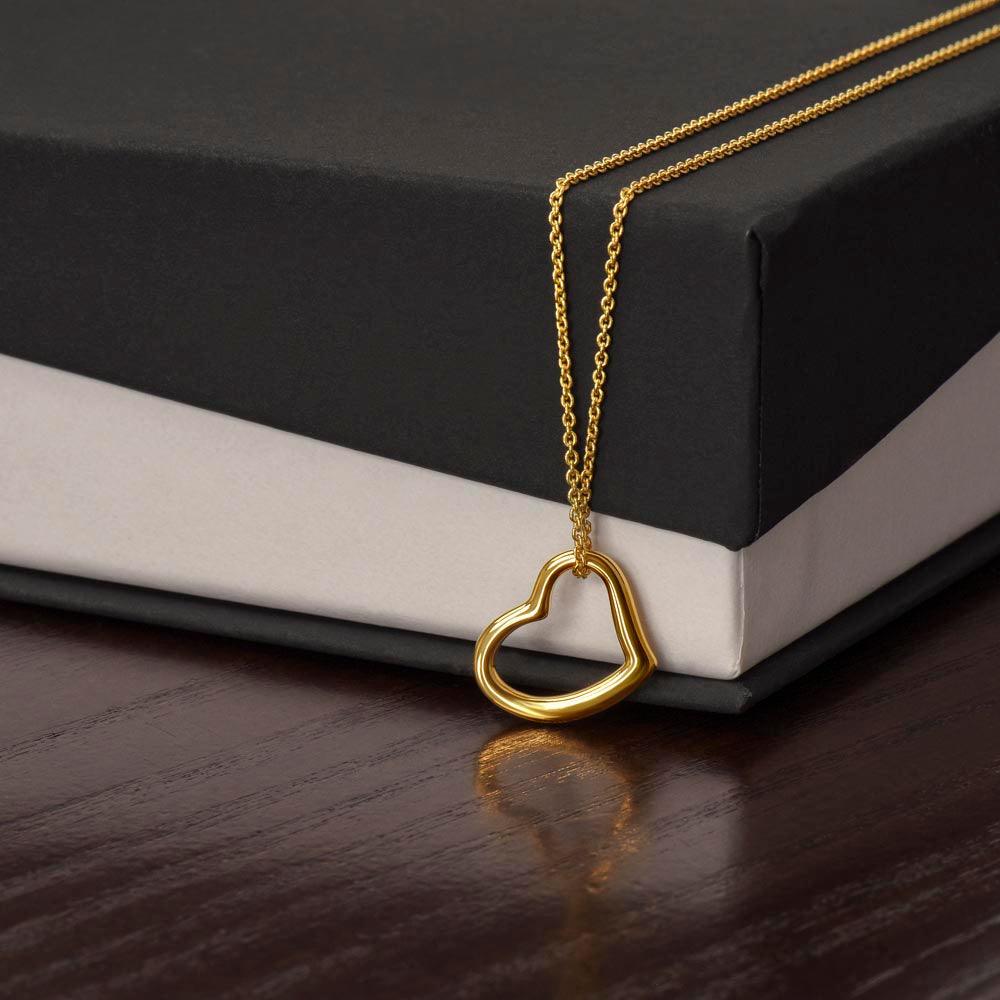 A Delicate Heart Necklace by Divine Dispatch in 14k white gold is elegantly displayed on a black and white gift box, placed on a dark wooden surface.